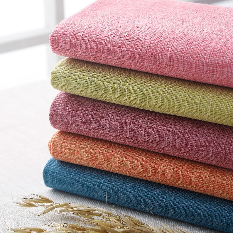May include: A stack of five fabric swatches in different colors: pink, green, burgundy, orange, and blue. The fabric has a textured, woven look.