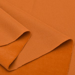 May include: Close-up of a folded piece of orange fabric. The fabric has a textured surface and a soft, fuzzy feel.