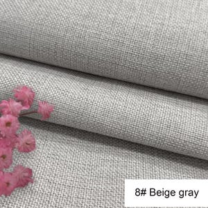 May include: A piece of beige grey fabric with a visible woven texture, folded to create horizontal layers. A small cluster of pink flowers is positioned on the left side. A white rectangular label displays the text 8# Beige grey.