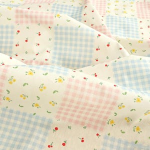 Peut inclure: Gros plan sur un tissu avec un motif patchwork. Le tissu présente des carrés de vichy bleu clair, de vichy rose et de tissu blanc avec de petites fleurs jaunes, des cerises rouges et des feuilles vertes.