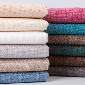 May include: A stack of fabric swatches in various colors and textures, including beige, white, gray, brown, teal, and pink. The swatches are folded neatly and arranged in a row.