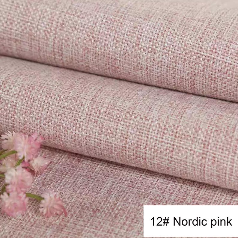 May include: A textured fabric in a soft pink hue with a visible woven pattern, folded into layers. Small, delicate light pink flowers are positioned in the lower left corner. The text 12# Nordic pink is printed in the bottom right corner.