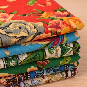 May include: A stack of six colorful fabric squares with floral and geometric patterns. The top square is red with large yellow and pink flowers. The second square is blue with a floral pattern. The third square is green with a geometric pattern. The fourth square is green with a floral pattern. The fifth square is blue with a paisley pattern. The bottom square is white with a floral pattern.