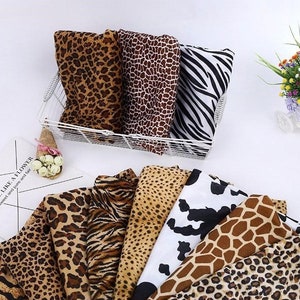 Könnte beinhalten: Sortiment von Stoffproben mit verschiedenen Tierdrucken, darunter Leopard, Zebra, Giraffe und Tigermuster. Die Proben sind in einem Drahtkorb und auf einer weißen Oberfläche angeordnet.