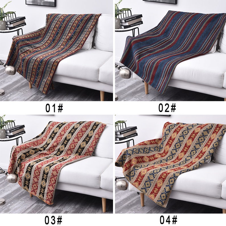 May include: Four different patterned throw blankets displayed on white sofas. The blankets are in various colors, including red, blue, black, and gold. The blankets have a striped pattern with geometric designs.