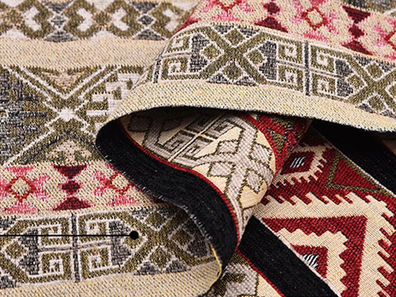May include: Close-up of a beige and brown woven rug with geometric patterns in shades of red, green, and black.