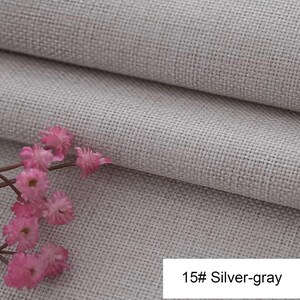 May include: A silver-grey fabric with a visible woven texture and a folded edge, accompanied by a small cluster of delicate pink flowers. A white rectangular label in the corner displays the text 15# Silver-gray in black lettering.