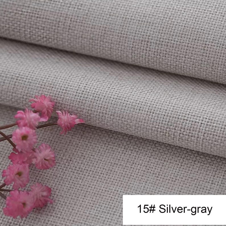 May include: A silver-grey fabric with a visible woven texture and a folded edge, accompanied by a small cluster of delicate pink flowers. A white rectangular label in the corner displays the text 15# Silver-gray in black lettering.