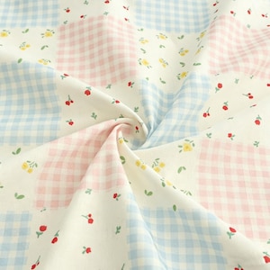 Könnte beinhalten: Nahaufnahme eines Stoffes mit Patchwork-Design. Der Stoff zeigt Quadrate aus hellblauem und rosa Vichy, durchsetzt mit weißen Quadraten, die mit kleinen gelben Blumen, roten Kirschen und grünen Blättern verziert sind. Der Stoff ist gefaltet und erzeugt weiche Kurven.