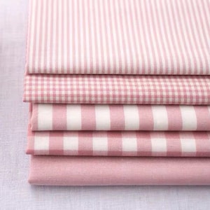 May include: A selection of pink and white fabric swatches. The patterns include vertical stripes, small gingham checks, wide stripes, and a plain pink fabric. The fabrics are neatly folded, displaying a range of textures and designs.
