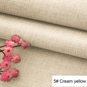 May include: A piece of cream yellow fabric with a visible woven texture and a grid-like pattern. A small cluster of delicate pink flowers with thin brown stems is positioned on the left side. The text 5# Cream yellow is visible in the corner.