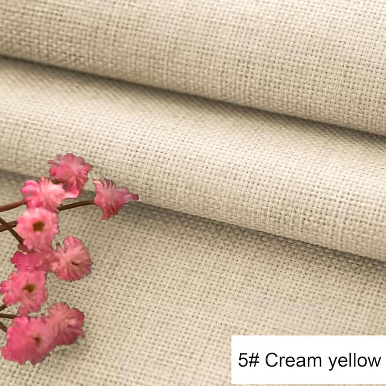 May include: A piece of cream yellow fabric with a visible woven texture and a grid-like pattern. A small cluster of delicate pink flowers with thin brown stems is positioned on the left side. The text 5# Cream yellow is visible in the corner.