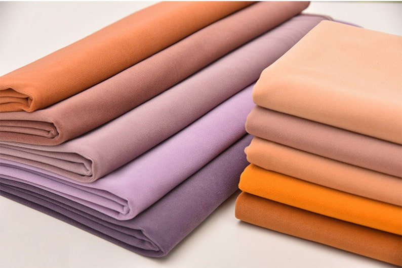 May include: A stack of fabric swatches in various shades of brown, purple, and orange. The fabric is soft and smooth, and the colors are muted and earthy.
