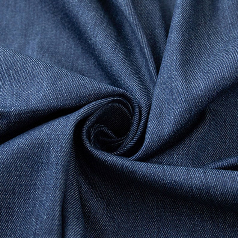 Op de afbeelding: Close-up van een donkerblauwe denim stof met een textuur geweven. De stof is gevouwen en gedrapeerd, waardoor de zachte en soepele textuur zichtbaar is.