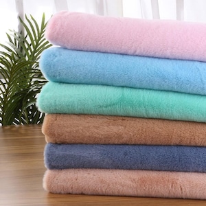 May include: A pile of soft, faux fur fabric in a range of pastel shades. The colours include pink, light blue, mint green, brown, navy blue, and a muted pink. The fabric looks fluffy and is likely for crafts or home decor.