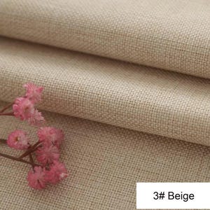 May include: A beige fabric with a visible woven texture folded into layers, accompanied by a small sprig of pink flowers. A white rectangular label in the corner displays the text 3# Beige in black font, indicating the colour of the material.