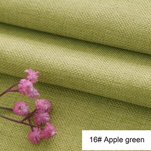 May include: Apple green fabric with a visible woven texture folded into layers. A small cluster of delicate pink flowers with thin stems rests on the surface. A white rectangular label in the corner displays the text 16# Apple green.