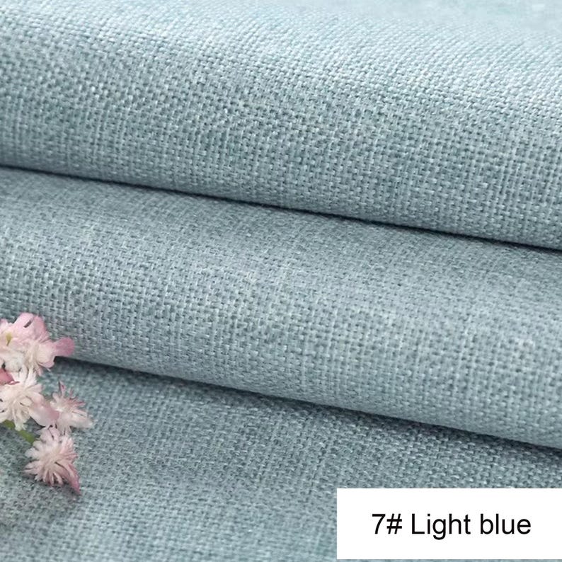 May include: A light blue fabric with a visible woven texture, folded into two horizontal layers. A small cluster of white and light pink flowers is positioned in the lower left corner. A white rectangular label displays the text 7# Light blue.