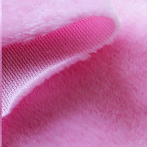 May include: Close-up of a pink fabric with a ribbed texture. The fabric is soft and fuzzy, with a subtle sheen.