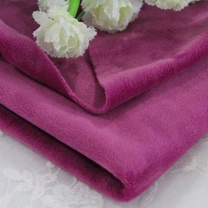 May include: A close-up of a soft, plush fabric in a deep purple hue. The fabric is folded in half, showcasing its texture and color.