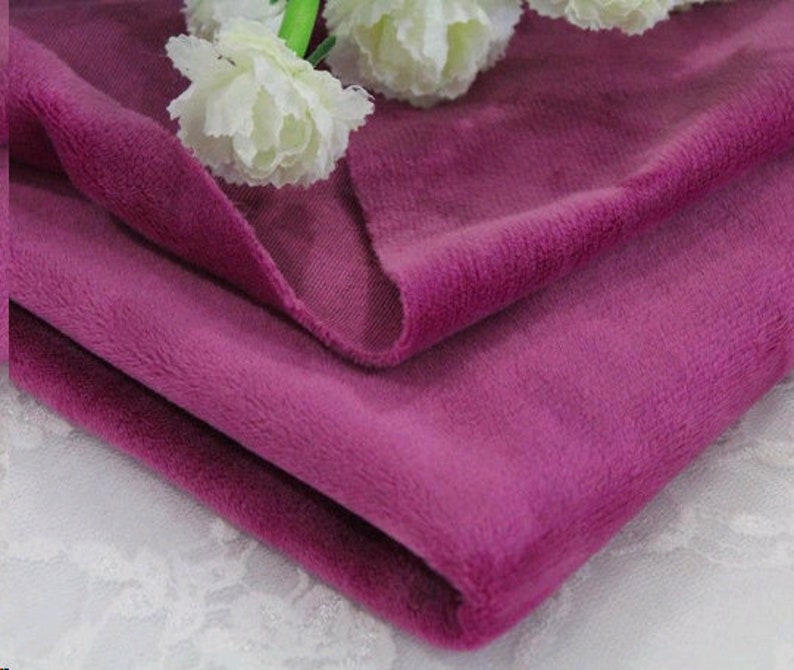 May include: A close-up of a soft, plush fabric in a deep purple hue. The fabric is folded in half, showcasing its texture and color.