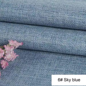 May include: A sky blue fabric with a visible woven texture and a grid-like pattern. The material is folded in layers, creating horizontal lines across the surface. A small cluster of light pink flowers is positioned on the left side. Text reads 6# Sky blue.