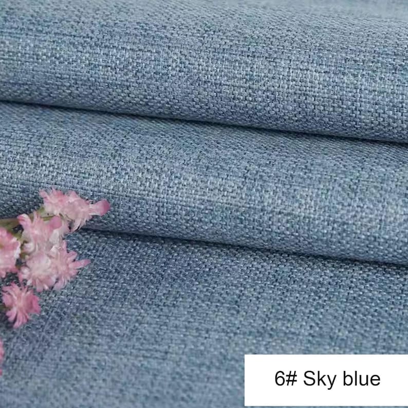 May include: A sky blue fabric with a visible woven texture and a grid-like pattern. The material is folded in layers, creating horizontal lines across the surface. A small cluster of light pink flowers is positioned on the left side. Text reads 6# Sky blue.