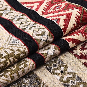 May include: Close-up of a woven fabric with a geometric pattern in shades of red, black, white, and gold. The fabric is folded over itself, showing the intricate details of the design.