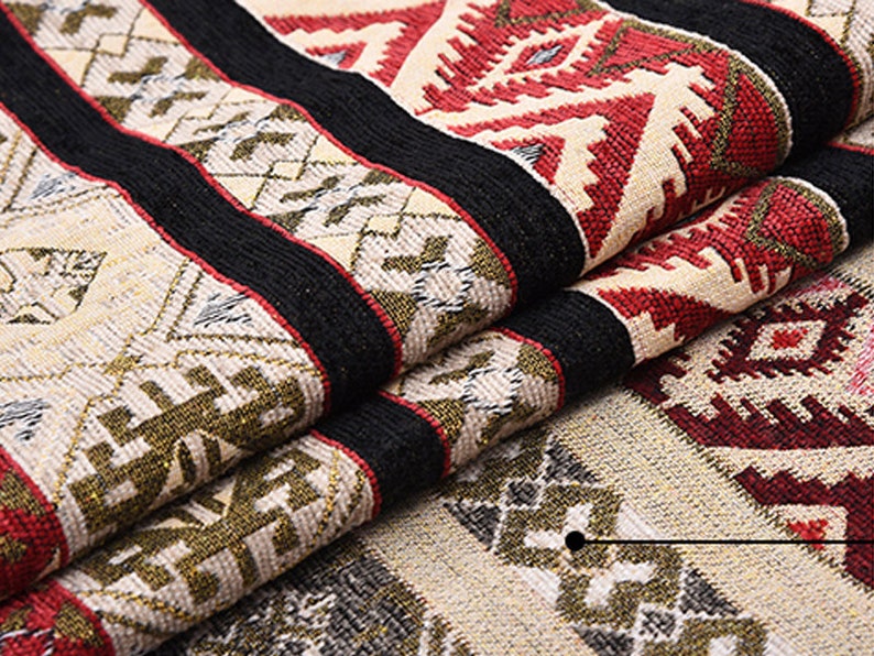 May include: Close-up of a woven fabric with a geometric pattern in shades of red, black, white, and gold. The fabric is folded over itself, showing the intricate details of the design.