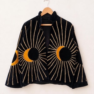 以下が含まれることがあります： フロントパネルと袖に金色の刺繍で三日月と太陽の光が施された黒いベルベットのジャケット。このジャケットはハイカラー、長袖、オープンフロントのデザインで、全体に精巧な刺繍が施されています。