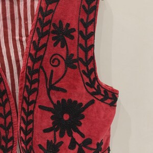 May include: A red velvet waistcoat with black embroidery of floral designs. The waistcoat has a striped lining.