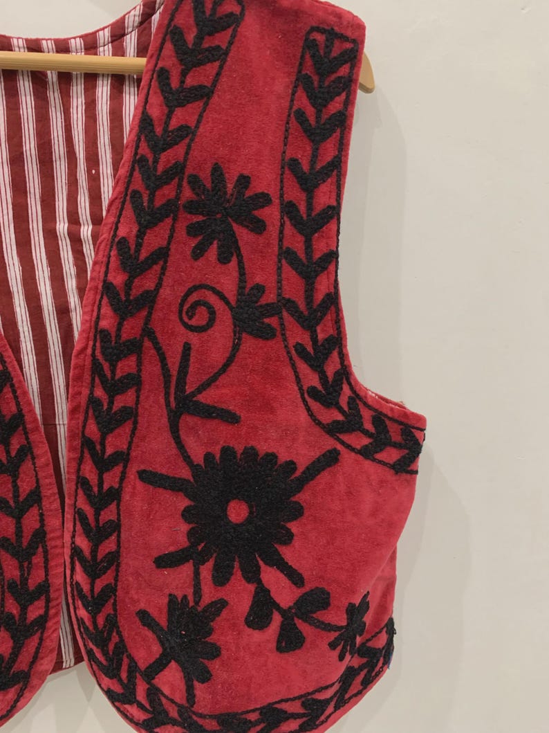 May include: A red velvet waistcoat with black embroidery of floral designs. The waistcoat has a striped lining.