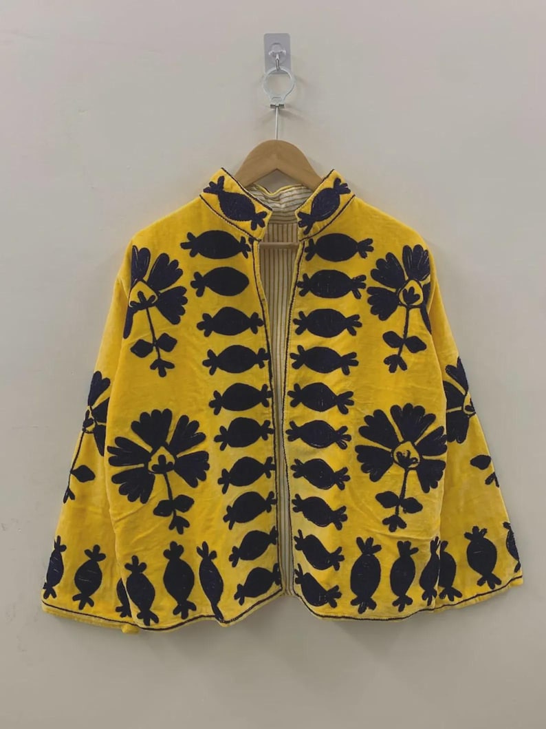 May include: A yellow jacket with a floral design in navy blue. The jacket has a mandarin collar and is open in the front. The floral pattern is repeated throughout the jacket. The jacket is hanging on a wooden hanger.