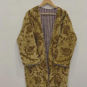 May include: A long-sleeved, open-front coat featuring a mustard yellow exterior with dark brown embroidered floral and pomegranate motifs. The interior lining and trim display a vertical brown and white striped pattern, with two front pockets.
