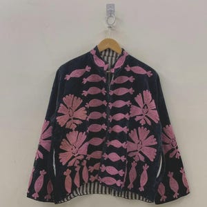 May include: A navy blue jacket with pink floral embroidery and candy-shaped designs. The jacket has a stand-up collar, long sleeves, and a striped lining. It is hanging on a wooden hanger.