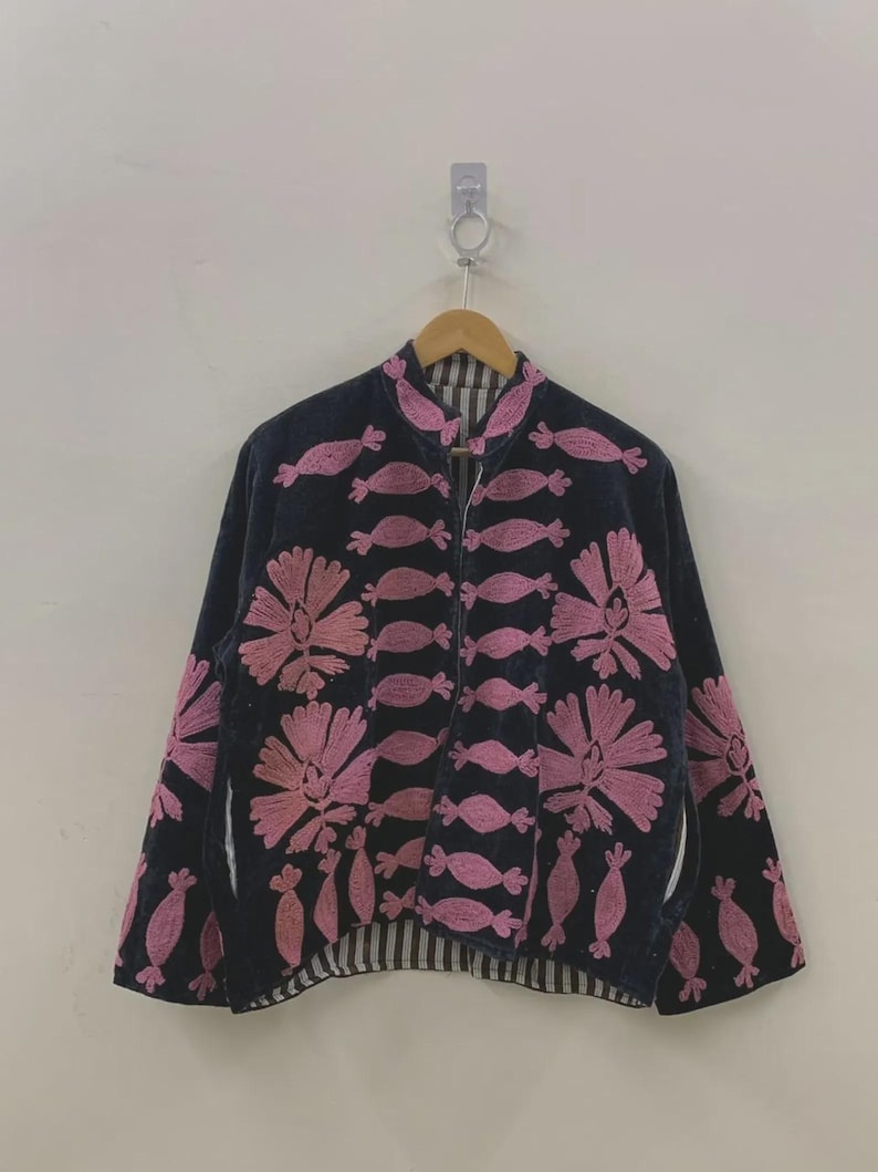 May include: A navy blue jacket with pink floral embroidery and candy-shaped designs. The jacket has a stand-up collar, long sleeves, and a striped lining. It is hanging on a wooden hanger.