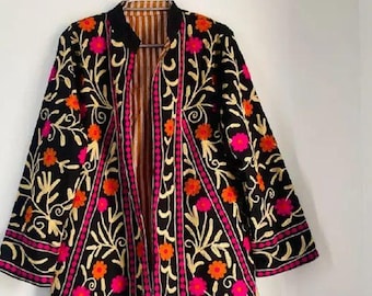 Puede incluir: Chaqueta negra bordada con motivos florales dorados, naranjas y rosas. La chaqueta tiene un interior a rayas y está colgada de una percha plateada. La chaqueta tiene cuello y mangas tres cuartos.