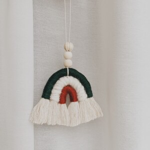 May include: A green, white, and red yarn rainbow with white tassels hanging from a white string with wooden beads.