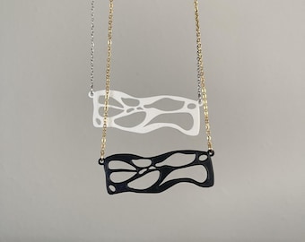May include: Two necklaces with abstract pendants. One has a white pendant on a silver chain, the other a black pendant on a gold chain. Both pendants have an open, flowing design.
