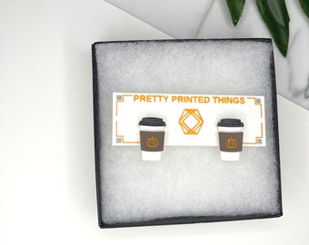 May include: A pair of white coffee cup earrings with a brown rim and a pumpkin design on the cup. The earrings are displayed on a white card with the text "PRETTY PRINTED THINGS".