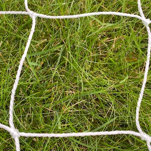 May include: White nylon soccer net with a square shape, against a background of green grass.