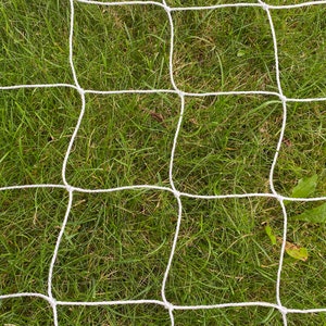 Może przedstawiać: Biała siatka rozciągnięta nad zielonym, trawiastym polem. Siatka jest wykonana z cienkiego, białego sznurka i utkana w wzór siatki.
