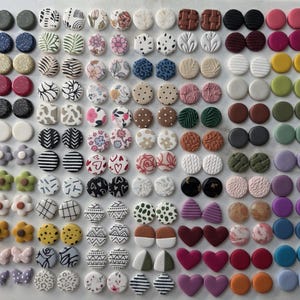 May include: A large collection of small stud earrings in various shapes, colors, and patterns, including circles, hearts, flowers, bows, and holiday-themed designs like gingerbread houses, Christmas trees, and Santa hats, arranged in a grid.