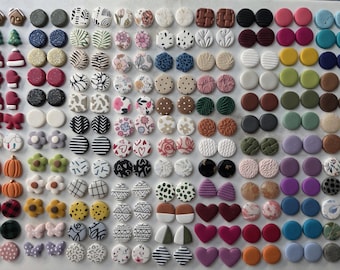 May include: A large collection of small stud earrings in various shapes, colors, and patterns, including circles, hearts, flowers, bows, and holiday-themed designs like gingerbread houses, Christmas trees, Santa hats, and pumpkins.