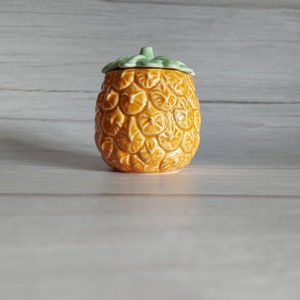May include: A ceramic pineapple-shaped jar with a green lid. The jar is yellow and has a detailed pineapple design.