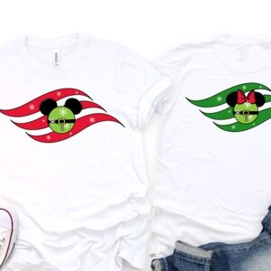 May include: Two white t-shirts featuring a Christmas-themed Mickey Mouse and Minnie Mouse design. The shirts display a red and green wave design with a Mickey Mouse head and a Minnie Mouse head in the centre. The Mickey Mouse head is wearing a Santa hat and the Minnie Mouse head is wearing a red bow.