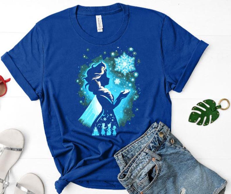May include: Royal blue t-shirt featuring a silhouette of a woman with a snowflake design. The graphic is in shades of blue and white. The shirt is made of a soft material and has short sleeves.
