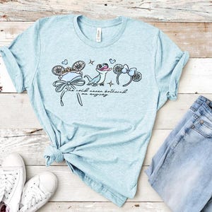 以下が含まれることがあります： ライトブルーの霜降りTシャツ。小さなトカゲ、リボン付きの装飾的な耳が2組、そして胸の中央に筆記体で「The cold never bothered me anyway」というテキストがグラフィックプリントされています。