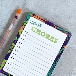 May include: A notepad with a colorful abstract design and the words "TODAY'S CHORES" printed in green. The notepad has a white lined section for writing a list of chores.