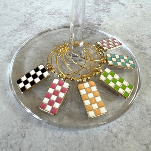 May include: Set of six gold-tone wine glass charms with checkered patterns in pink, green, black and white, orange and white, and blue and white.